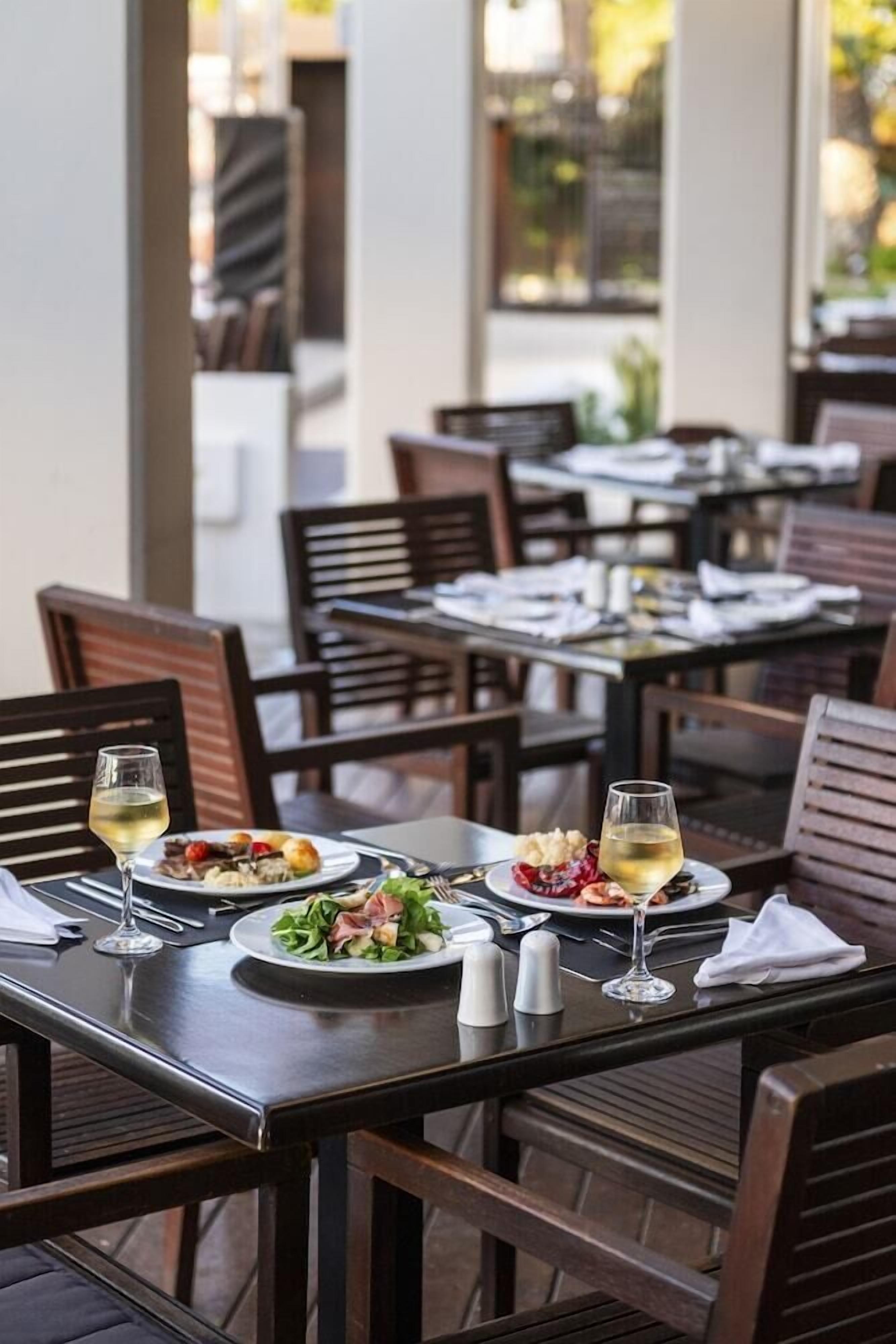 Um restaurante com mesas preparadas para refeições, cada uma com um prato de comida, um copo de vinho e talheres.