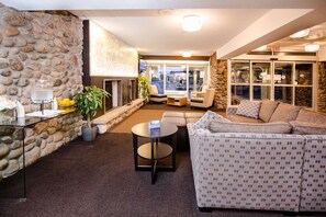 A cozy interior with a stone wall, a fireplace, a seating area with a sofa and chairs, and a glass door leading outside. - Ottawa Kanata Hotel and Conference Centre (Ottawa)