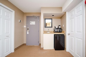 A hotel room with a kitchenette, a door with a lock, a small mirror, and a trash bin. - Ottawa Kanata Hotel and Conference Centre (Ottawa)