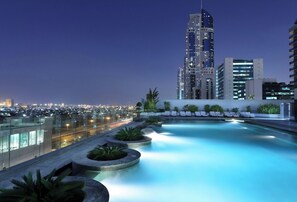 A rooftop pool with lounge chairs and a cityscape view at dusk.