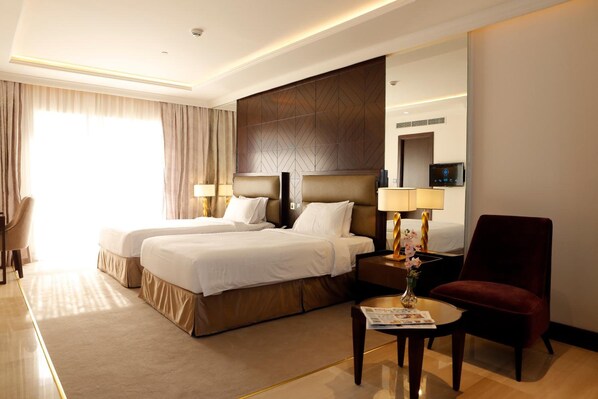 A hotel room with two beds, a desk, a chair, a lamp, and a mirror.