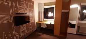 A compact room with a bed, a desk, a chair, a TV, and a window with curtains. - Sure Hotel Spanga (Spånga)