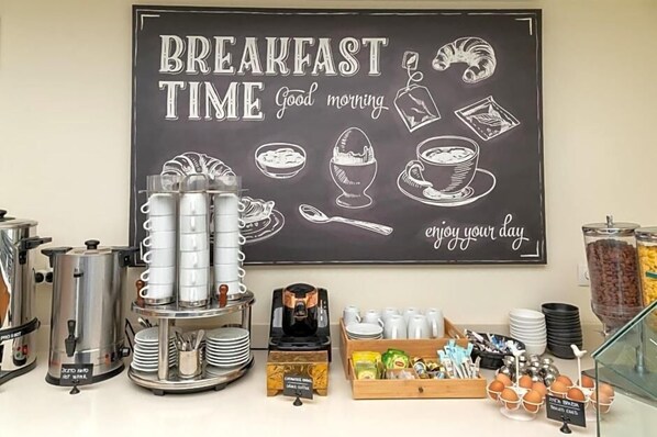 A breakfast setup with a chalkboard sign, coffee machines, and food items.