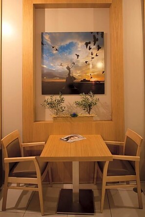 Un coin repas avec une table et des chaises en bois, un tableau encadré au mur et une petite plante posée sur la table.
