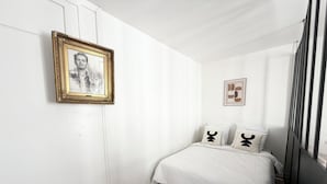 Ein Schlafzimmer mit einem Bett, weißen Wänden, einem gerahmten Bild und einem Fenster.