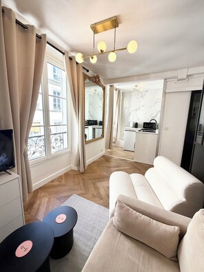 Ein modernes Wohnzimmer mit einer Couch, einem Fernseher und einem Essbereich, im Hintergrund eine Küche.