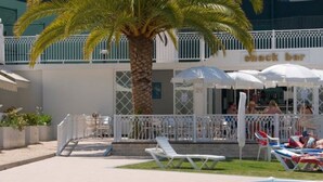 A pool area with lounge chairs, a palm tree, and a shack bar. - Tropical Sol (Albufeira)