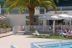 Uma área de piscina com espreguiçadeiras, uma palmeira e um bar simples.