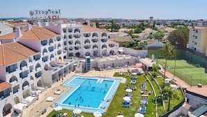 A hotel with a large swimming pool, multiple balconies, and a tennis court. - Tropical Sol (Albufeira)