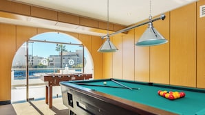 A pool table with balls, a pool cue, and a table lamp in a room with wooden paneling and a large window. - Tropical Sol (Albufeira)