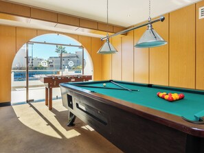 A pool table with balls, a pool cue, and a table lamp in a room with wooden paneling and a large window. - Tropical Sol (Albufeira)