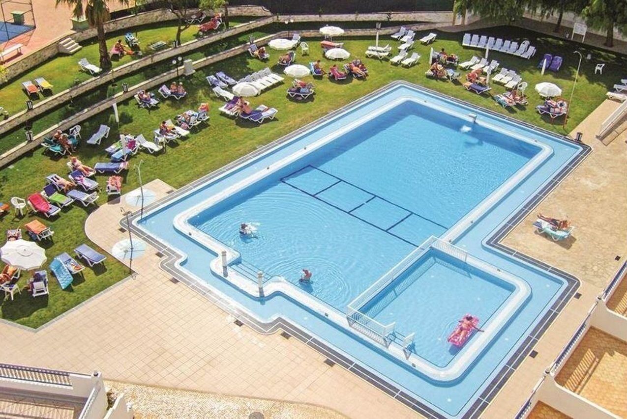 A large rectangular swimming pool with multiple lanes, surrounded by sun loungers and umbrellas.
