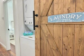 Señal de lavandería en una puerta de madera, una lavadora blanca y una cesta azul.