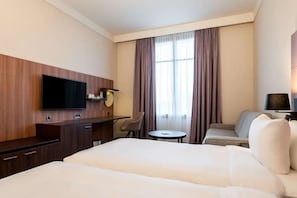 A hotel room with a large bed, a desk with a flat-screen TV, a chair, a small round table, and a sofa. - Hotel Paris Marne-la-vallee (Magny-le-Hongre)