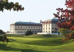 A large, multi-story building with a flat roof and multiple windows, situated on a grassy hill with trees in the foreground. - Crowne Plaza Paris Marne-la-vallée by IHG (Magny-le-Hongre)