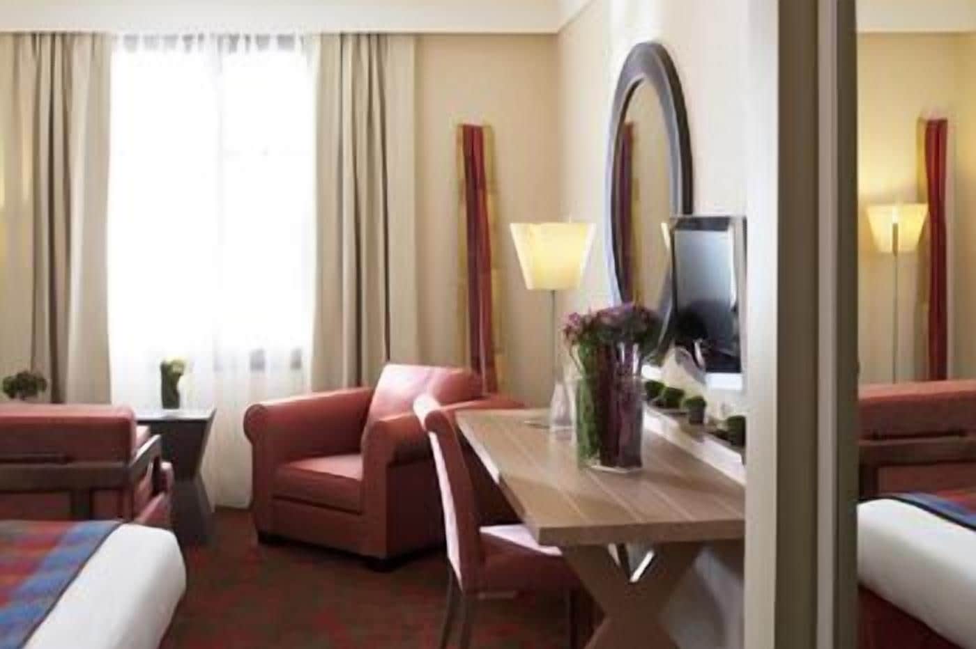 Une chambre d’hôtel avec un lit, un bureau, une chaise, une télévision et une fenêtre avec des rideaux.