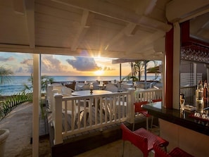 En restaurant ved havet med udendørs siddepladser, en bar og havudsigt i solnedgang.