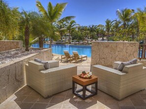 A poolside area with wicker furniture, a small table with a fruit bowl, and a stone wall. - TAN Resorts Marina Cap Cana (Punta Cana)