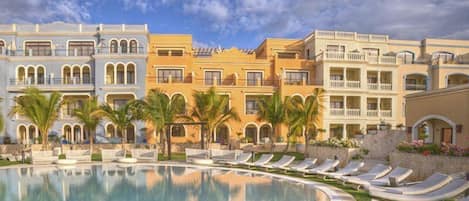 A hotel with a swimming pool, lounge chairs, and palm trees.