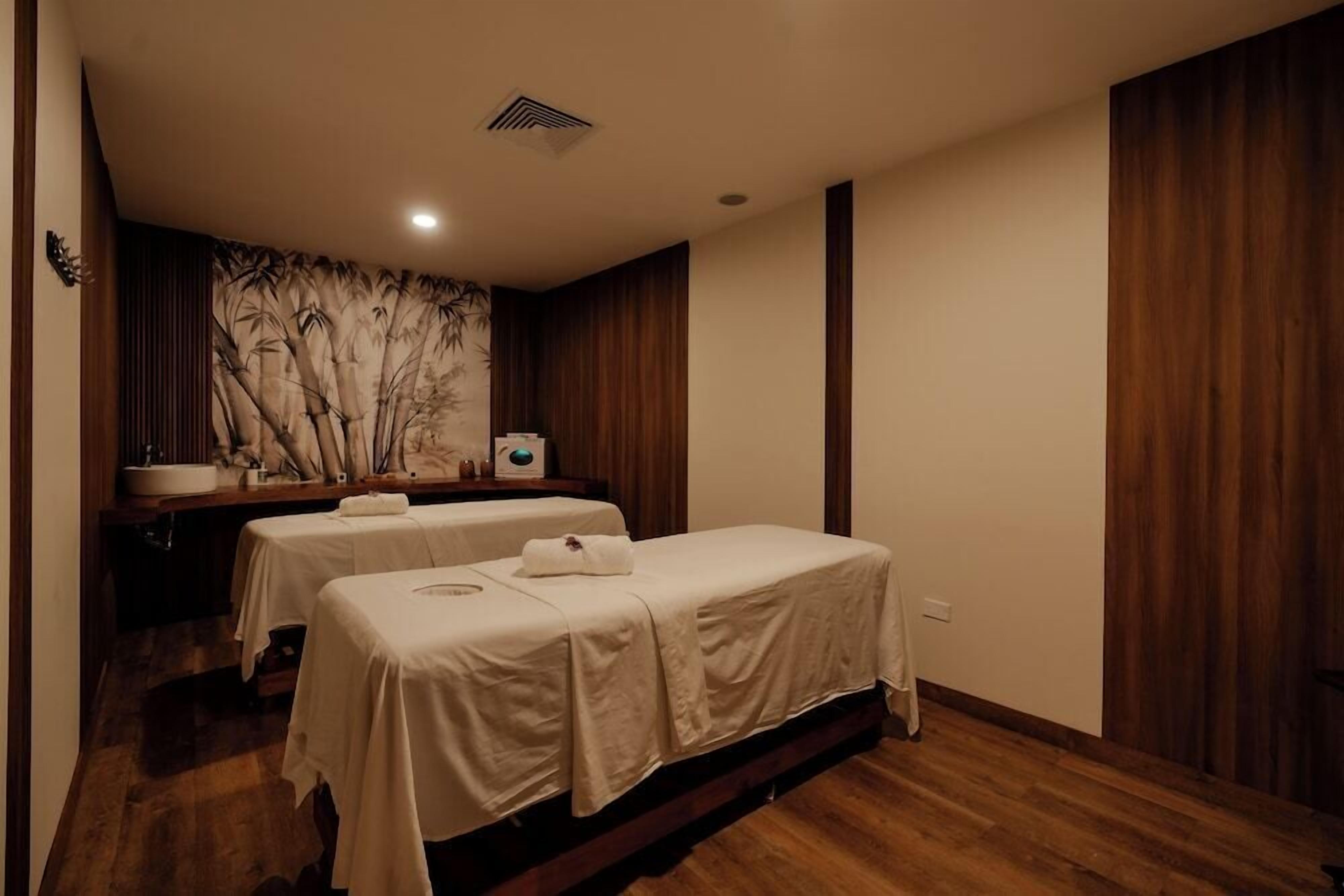 A room with two beds, a large mirror, a wooden floor, and a wall with a bamboo pattern.