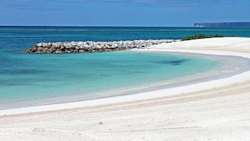 Une plage à l’eau turquoise et limpide, avec un rivage sablonneux et une digue rocheuse.