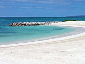 A beach with clear turquoise water, a sandy shore, and a rocky breakwater. - TAN Resorts Marina Cap Cana (Punta Cana)