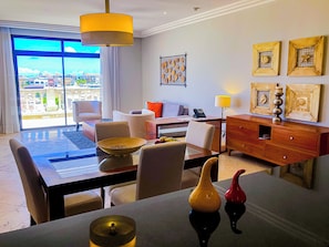 A hotel room with a dining area, a sofa, a desk, and a view of the city. - TAN Resorts Marina Cap Cana (Punta Cana)