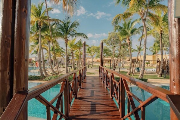 A wooden bridge leading to a pool surrounded by palm trees. - TAN Resorts Marina Cap Cana (Punta Cana)