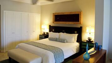 Une chambre d’hôtel avec un grand lit, deux tables de chevet avec des lampes, un ventilateur de plafond et une tête de lit en bois.