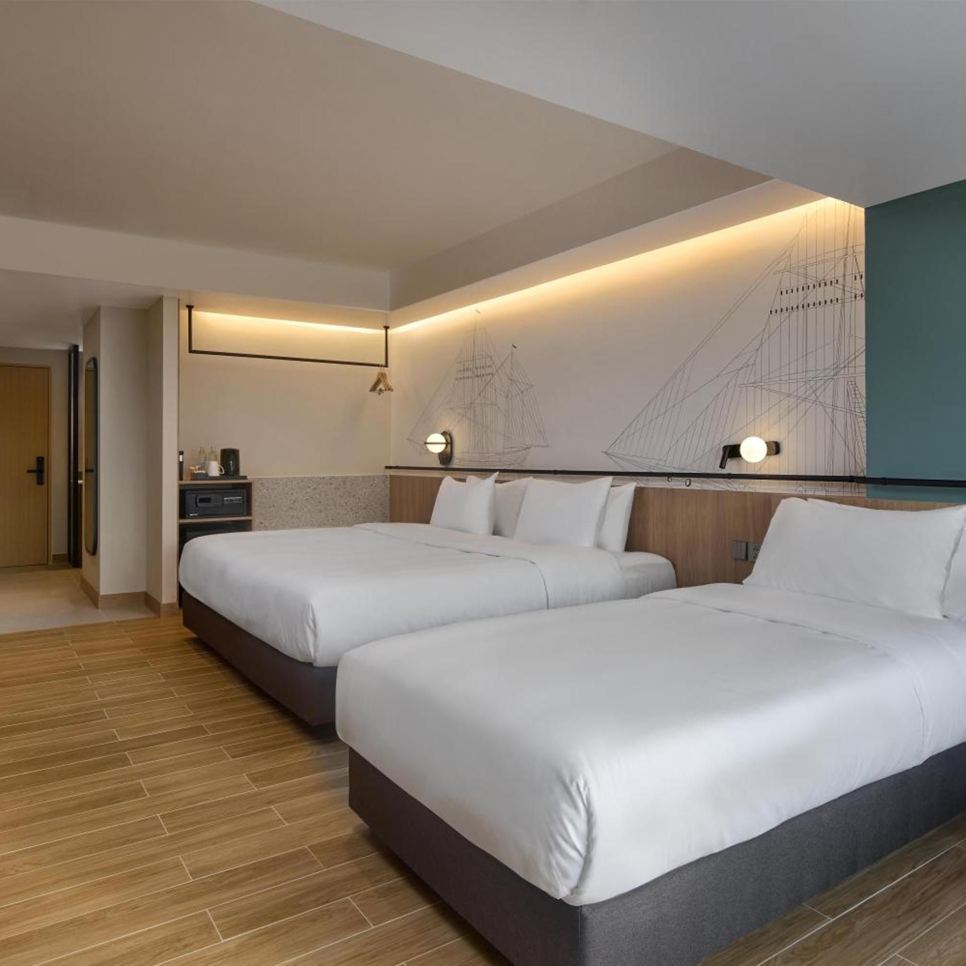 Habitación de hotel con dos camas, suelo de madera, un escritorio con silla y una pared con un cuadro de temática náutica.