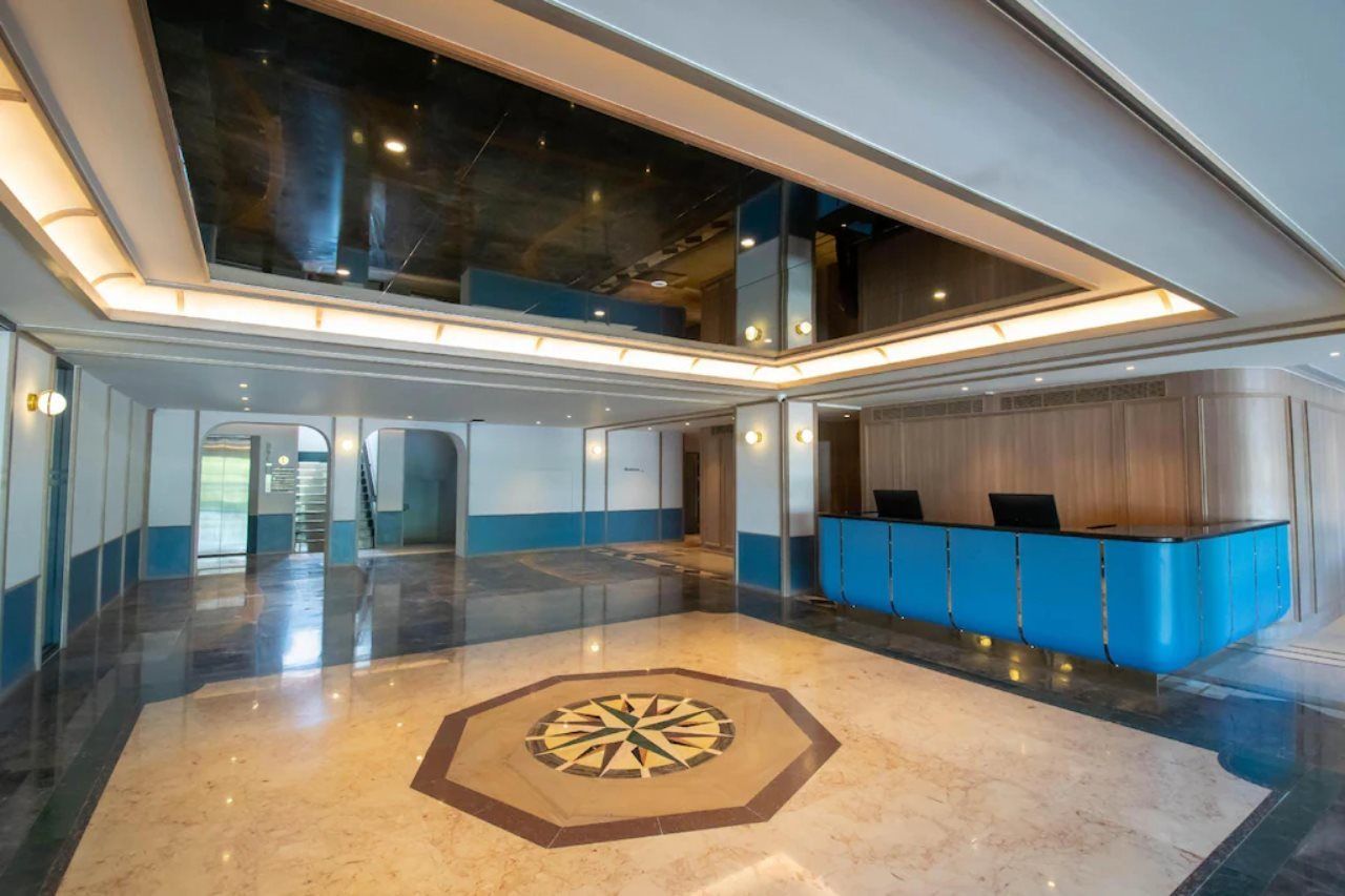A spacious lobby with a reception desk, a geometric floor design, and a high ceiling with skylights.