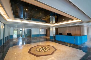 Un hall d’entrée spacieux avec un comptoir de réception, un motif géométrique au sol et un plafond haut doté de lucarnes.