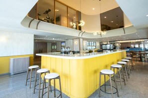 Una cocina moderna con una isla central, taburetes de bar y un techo alto con una lámpara original.