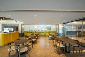 Un espace repas moderne avec des tables et des chaises, une cuisine en arrière-plan et une cloison en verre.
