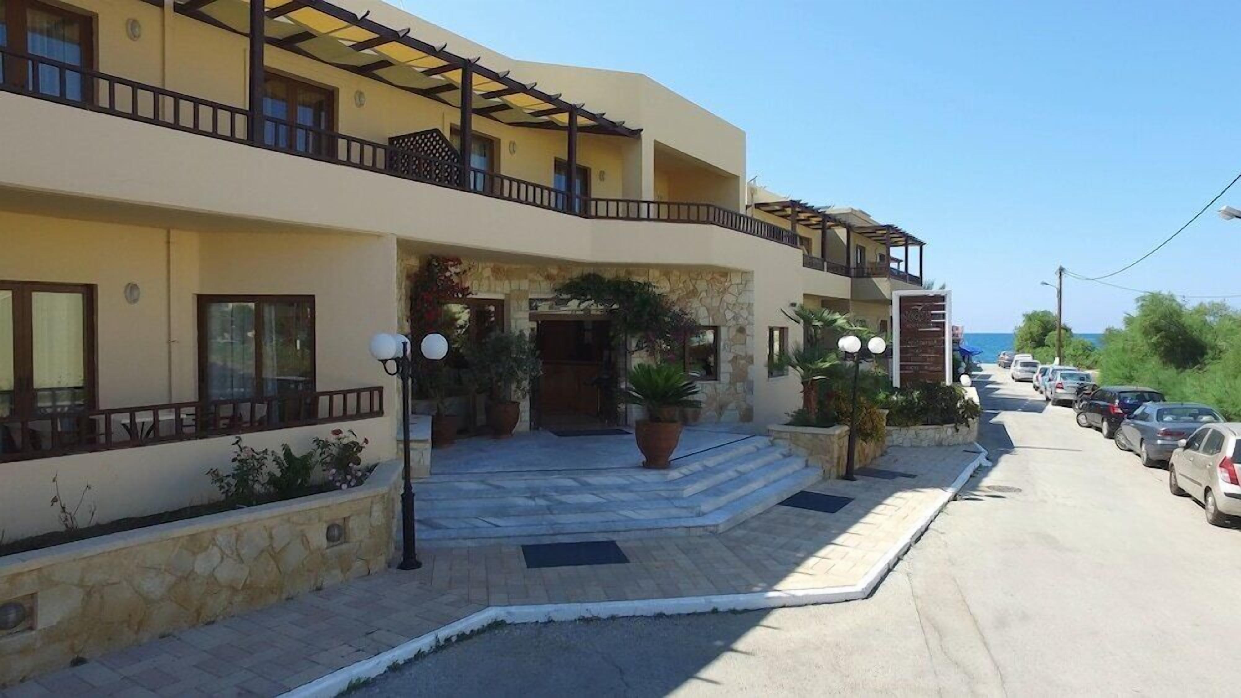 A two-story hotel with a stone facade, a covered entrance, and a parking lot with cars.
