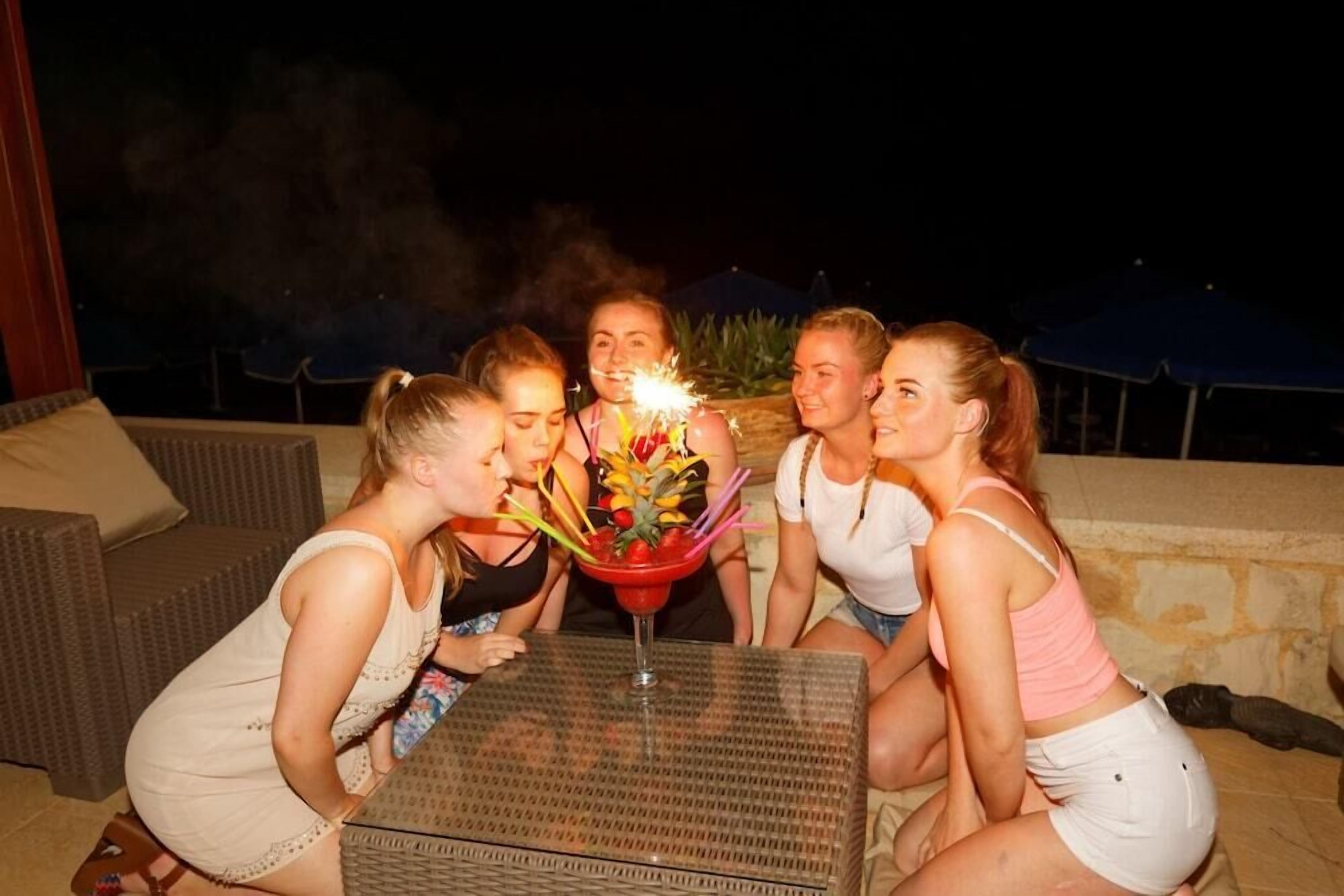 Un groupe de personnes s’est réuni autour d’une table, boissons à la main, à l’extérieur, pendant la nuit.