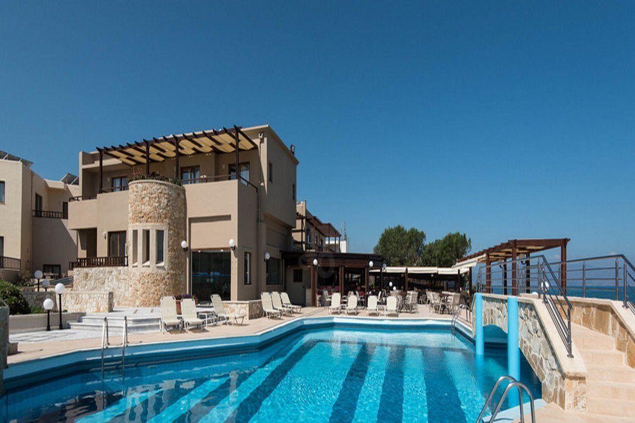 Un espace piscine avec des chaises longues, un pilier en pierre et un bâtiment doté de balcons.