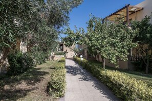 A pathway flanked by well-maintained hedges and trees, leading to a building with a balcony. - Indigo Mare (Platanias)
