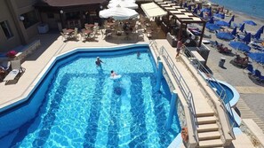 A swimming pool with a sun deck, lounge chairs, and umbrellas. - Indigo Mare (Platanias)