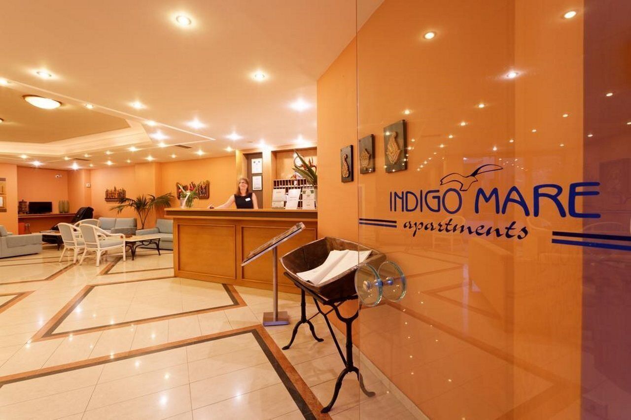 A hotel lobby with a reception desk, seating area, and a wall with the name 'INDIGO MARE apartments'.