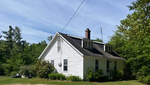 A white single-story house with a gabled roof, a chimney, and a small porch. - Quaint 3-bedroom farmhouse in peaceful Mason, NH. (Mason)