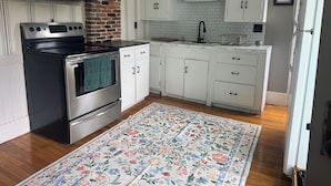 A kitchen with white cabinets, a stainless steel oven, a microwave, and a brick wall. - Quaint 3-bedroom farmhouse in peaceful Mason, NH. (Mason)