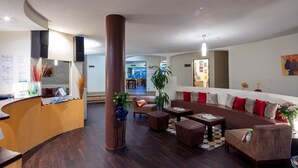 A modern lobby with a reception desk, a large central column, a sofa set, and a dining area in the background. - Noemys Toulon La Valette (La Valette-du-Var)