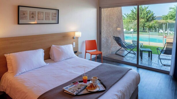 A hotel room with a bed, a tray with breakfast, a chair, and a view of a swimming pool. - Noemys Toulon La Valette (La Valette-du-Var)
