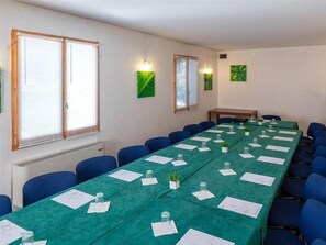 Un salón de conferencias con una larga mesa, sillas azules y manteles verdes.
