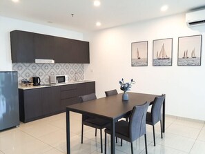 A modern kitchen with dark cabinetry, a microwave, and a coffee maker. There is a dining table with four chairs and a vase with flowers. Three framed pictures of sailboats are on the wall. - The Straits Johor Bahru (Johor Bahru)