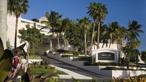 Entrada de un hotel con un cartel que dice 'MELIA NASSAU BEACH', rodeada de palmeras y un jardín bien cuidado.