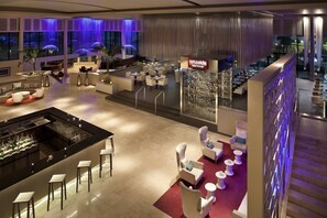 Um saguão moderno de hotel com área de bar, espaços de estar e vista para o terraço externo.
