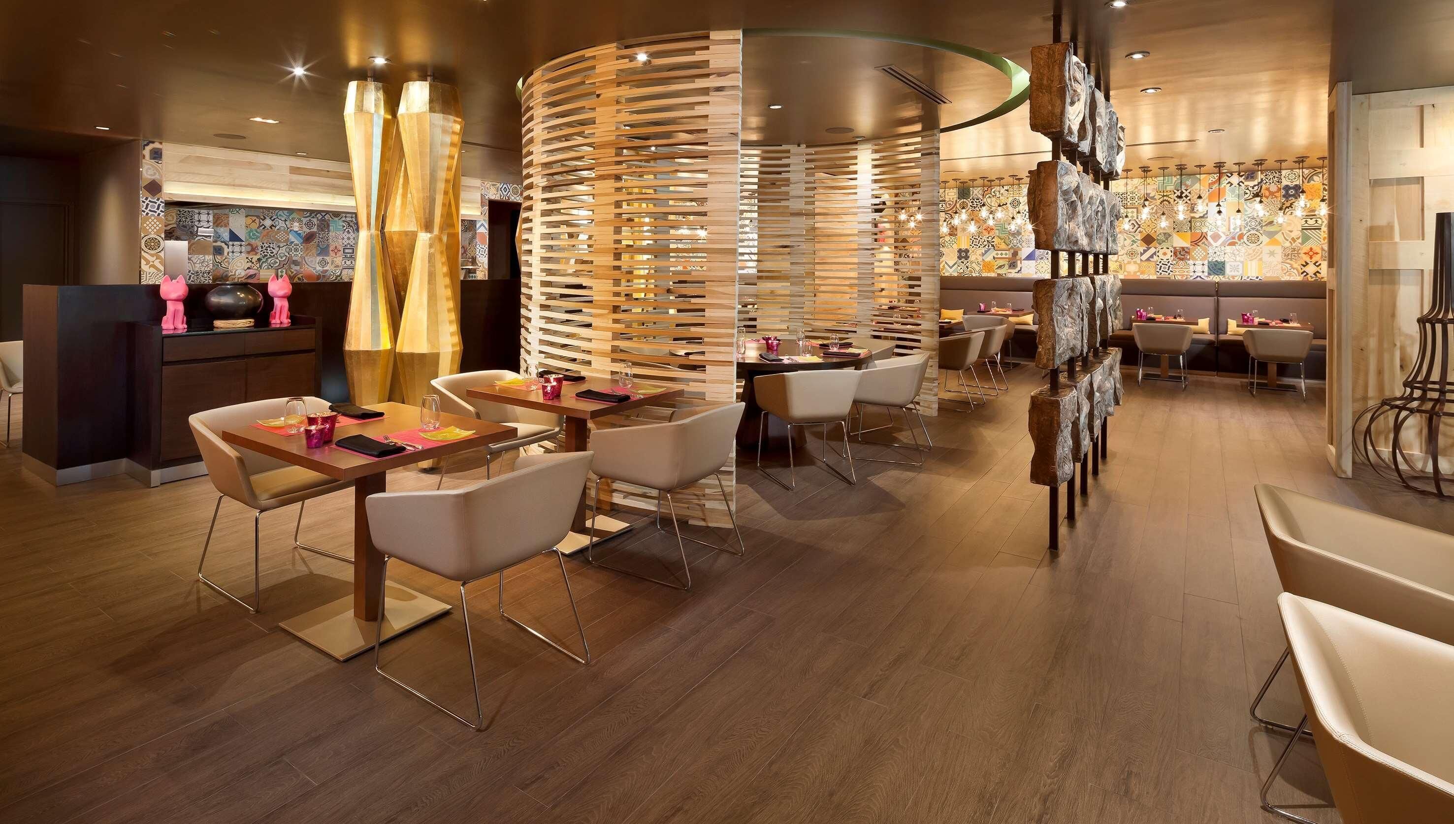 A modern restaurant interior with wooden slatted partitions, white chairs, and a patterned tile backsplash.