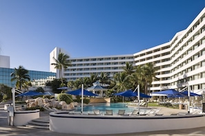 Um hotel com área de piscina, palmeiras e guarda-sóis azuis.